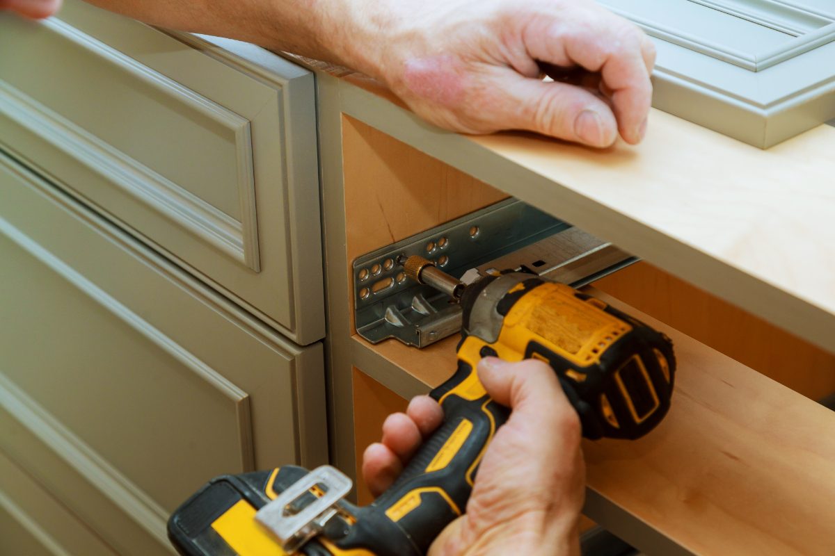 Technician installing cabinet hardware using a power drill on a kitchen cabinet door