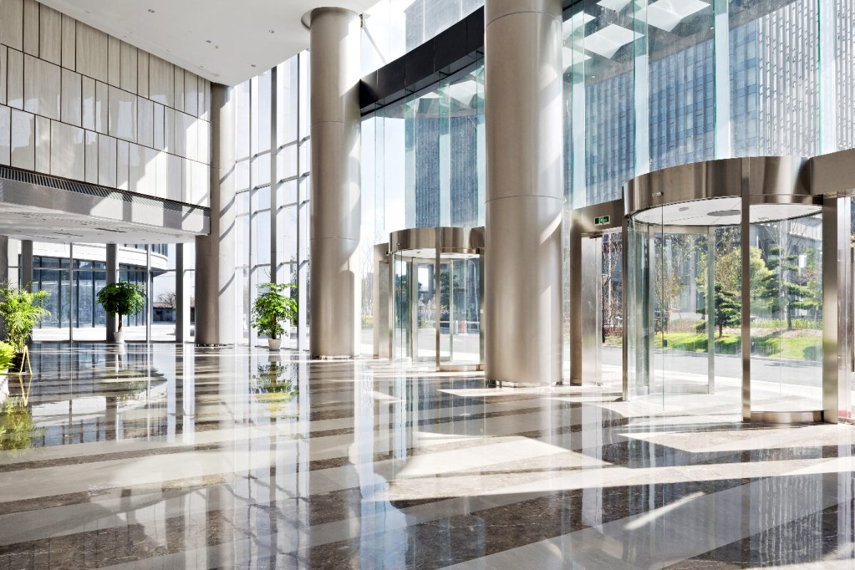 Modern office lobby with polished floors, tall columns, glass elevators, and floor-to-ceiling windows overlooking city skyline