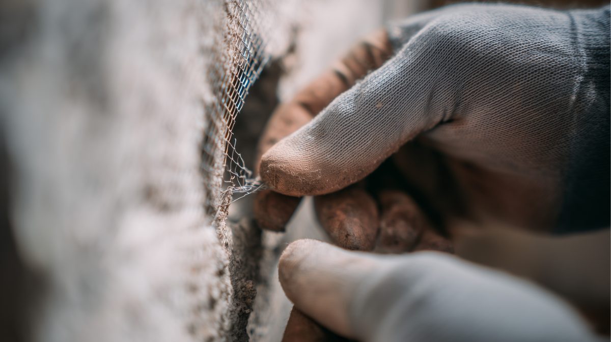 Close-up of hands applying mesh tape to drywall joint during construction